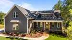 A modern gray house with white trim at 65 Stream View Way, Zebulon, features large windows and a covered front porch. Landscaped plants and trees surround the home, while a concrete path leads to the inviting front door.