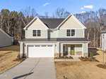 Charming two-story suburban house at 135 Vast View Way, Youngsville, with light green siding, white trim, black shingled roof, double garage, and a green front door. The mostly bare yard with small shrubs is set against a backdrop of trees.