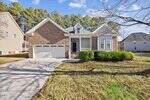 A modern brick and siding house at 8 Larkspur Court in Youngsville, featuring a two-car garage, front porch, large windows, and driveway, nestled among green grass, shrubs, and neighboring homes with tall trees in the background.