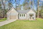 Charming single-story gray house at 133 Mohawk Drive, Louisburg, with an attached garage, white trim, and a covered front porch. Surrounded by tall trees and grass with a concrete driveway leading to the garage.
