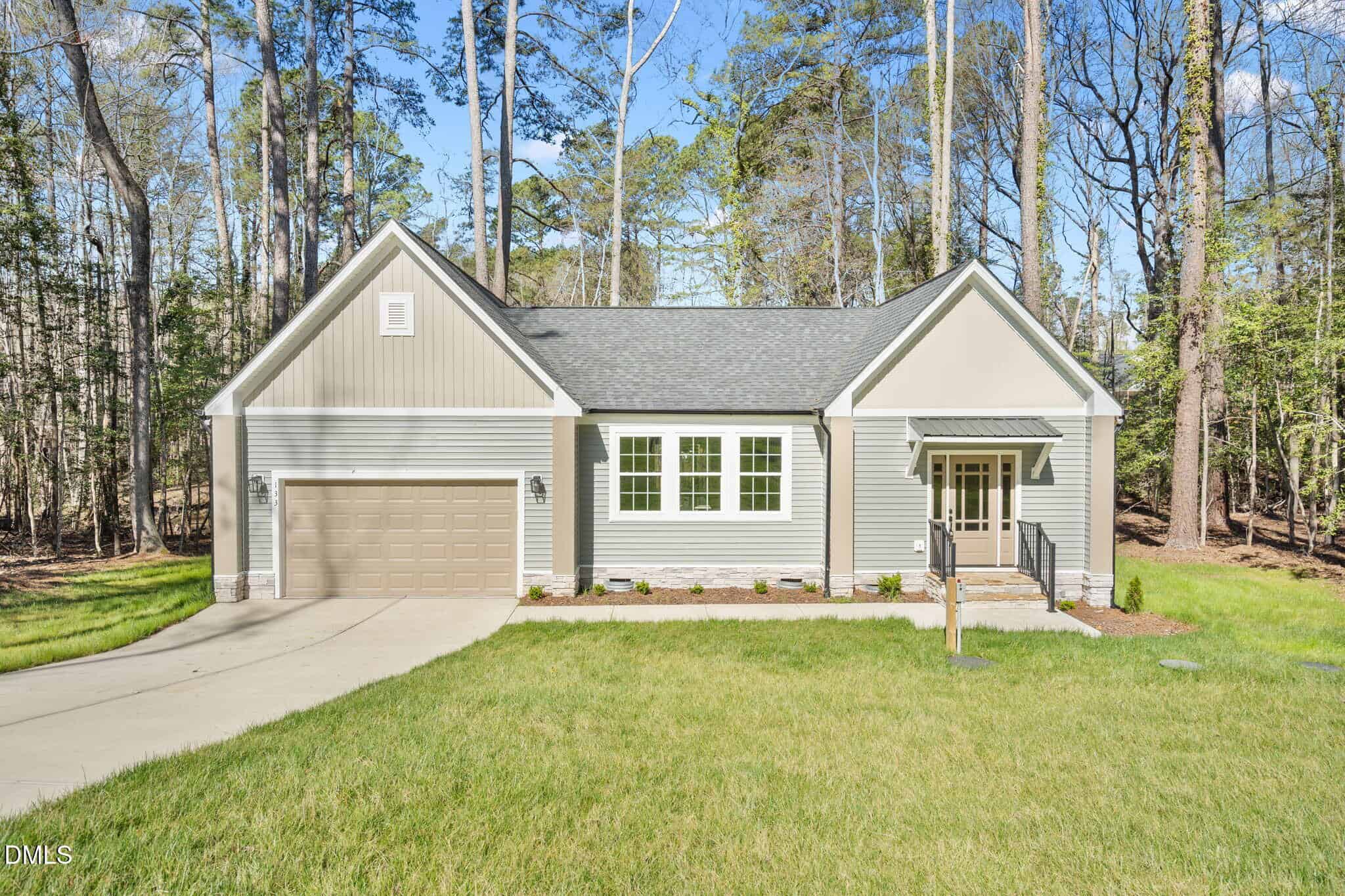 Charming single-story gray house at 133 Mohawk Drive, Louisburg, with an attached garage, white trim, and a covered front porch. Surrounded by tall trees and grass with a concrete driveway leading to the garage.