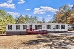 Located at 70 Rough Lane in Louisburg, this single-story manufactured home features white siding, red trim, a red front porch with a wheelchair ramp, star decorations, and multiple windows nestled among trees under a blue sky.