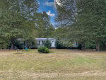 A single-story white house with a gray roof sits among tall trees at 45 Horsecreek Road in Louisburg, featuring a large, grassy front yard, a small birdbath, and various shrubs near the entrance under a partly cloudy sky.