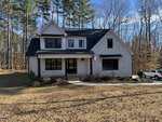 A two-story modern house with white siding and stone accents, black trim, and a covered front porch sits at 1124 Dovefield Lane in Youngsville. An American flag hangs by the entrance, with a car parked on the driveway amid trees and a grassy yard.
