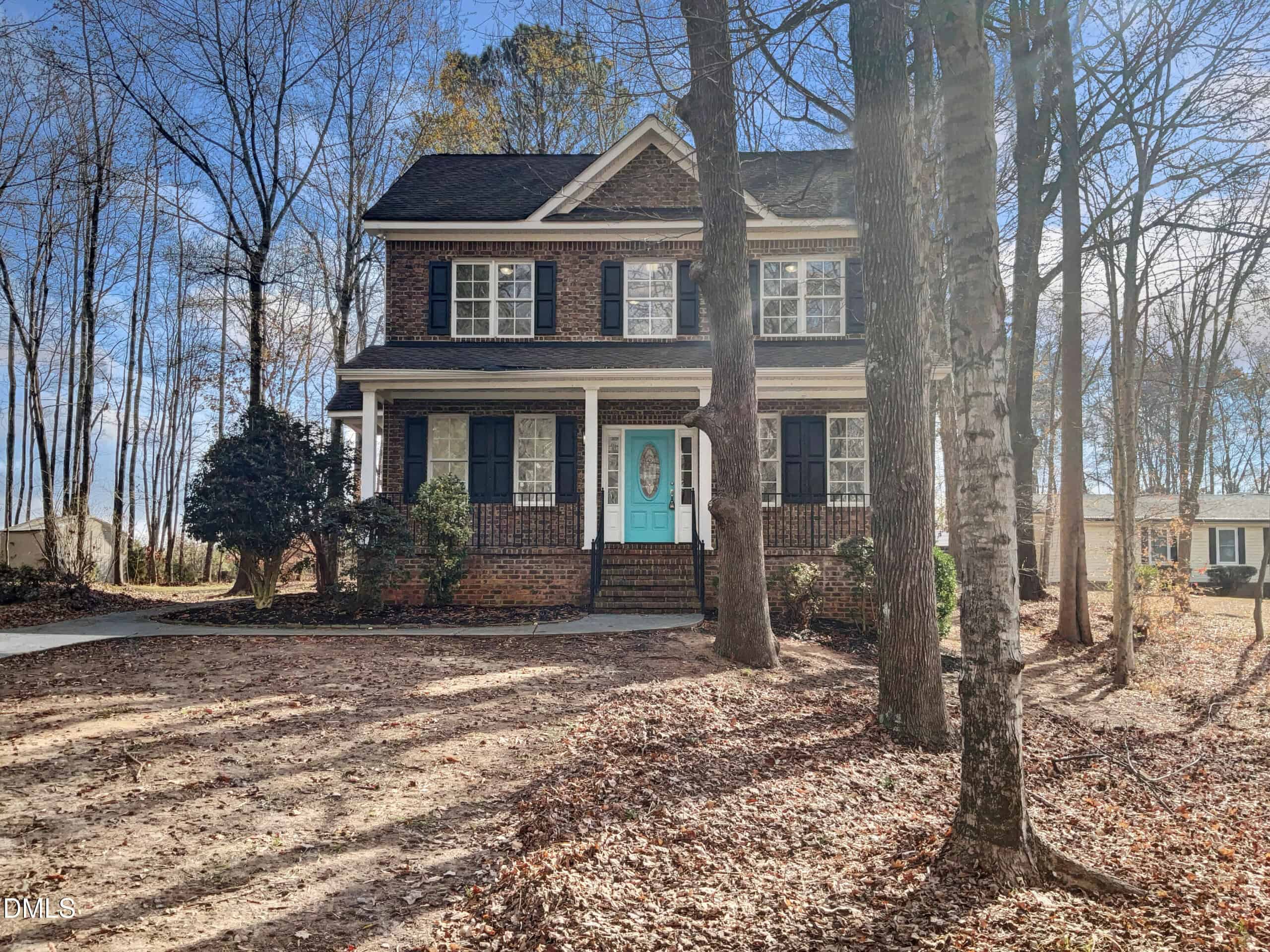 Charming two-story brick house in Franklinton with black shutters, a covered front porch, and a turquoise front door at 4445 W River Road, surrounded by tall trees and a leaf-covered yard on a sunny day.