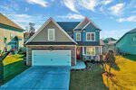 Charming two-story suburban house at 430 Stephens Way, Youngsville, featuring blue siding, stone accents, and a two-car garage. The front porch with chairs overlooks a manicured lawn, driveway, and neighboring homes under a clear blue sky.