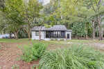 A small, single-story house with white walls and dark trim sits surrounded by trees and greenery at 302 Tar River Avenue in Louisburg. The front yard features shrubs and a mulch bed, with a wooded area in the background.