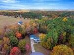 Aerial view of a house at 195 Woodcroft Drive, Youngsville, with a long driveway surrounded by autumn-colored trees in a rural neighborhood, open fields, and more homes in the distance under a blue sky.