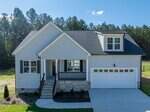 A modern, light-gray house at 95 Purslane Drive in Franklinton features a front porch, black shutters, two-car garage, stone accents on the foundation, and a neatly landscaped yard set against tall trees and clear blue sky.