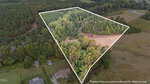 Aerial view of 305 Leghorn Drive in Zebulon outlined in white, showing dense trees, a dirt path, and cleared areas. Surrounded by other forested and open lands with nearby houses. Note: property lines are approximate.