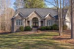 This single-story brick house at 2032 Silverleaf Drive in Youngsville features arched windows, a dark double front door, and a gabled roof. Surrounded by trees and a tidy lawn, it also offers a two-car garage on the right.