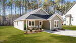 Charming single-story house at 108 Wichita Way, Louisburg, with gray siding, white trim, and a dark roof. Enjoy the covered front porch, landscaped yard, concrete driveway, and pine trees set under a clear blue sky.