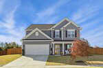 This two-story gray suburban house at 10 Cutshaw Road in Youngsville features white trim, a double garage, and a front porch. A small tree with red leaves graces the yard beneath the clear blue sky.