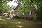 A brick house at 205 Fox Run Road in Youngsville features a porch with white railing, dark shutters, and is surrounded by trees and bushes, with a small white shed in the background and a curved sidewalk leading to the entrance.
