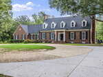 A large brick house with white trim, black shutters, multiple dormer windows, and an American flag by the front door sits at 270 Wiggins Road in Louisburg, surrounded by trees and a circular driveway in front.