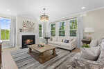 Bright living room at 255 Sugar Pine Drive in Franklinton with large windows, beige walls, a fireplace with art above it, a cream sofa, an armchair with a patterned pillow, wooden coffee table, and striped rug on light wood floors.
