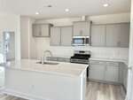 Modern kitchen at 10 Gerrard Street in Franklinton features gray cabinets, stainless steel appliances, built-in microwave, gas stove, white subway tile backsplash, and a large island with sink. Light wood floors and bright lighting throughout.