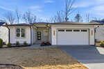 Modern single-story house at 646 Shawnee Drive, Louisburg, with white siding, a two-car garage, and a covered front entrance. The yard features minimal landscaping with brown grass and a few shrubs; leafless trees stand under a blue sky.
