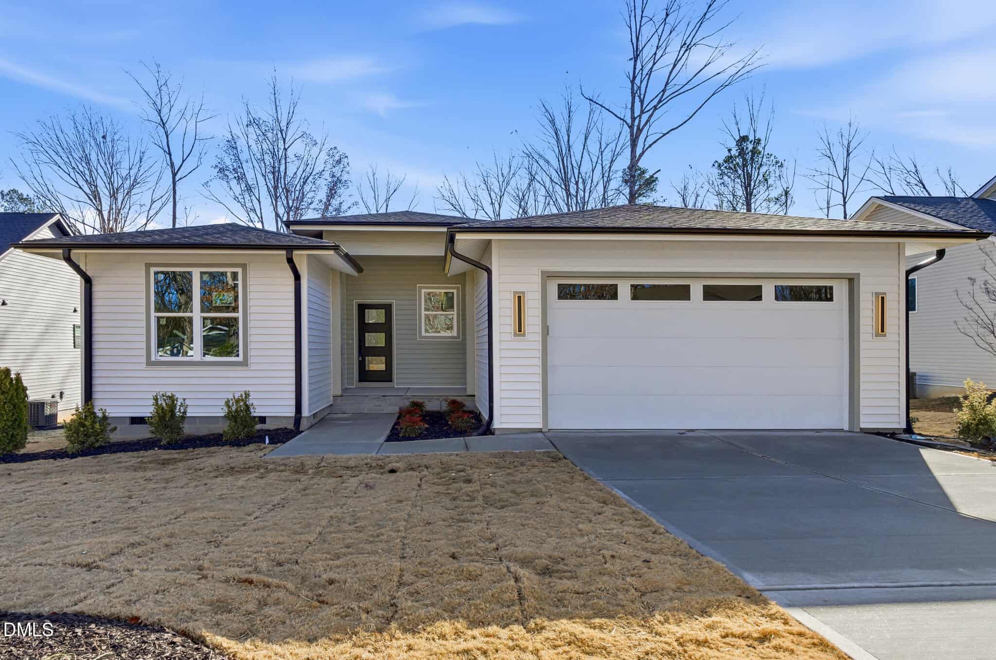 Modern single-story house at 646 Shawnee Drive, Louisburg, with white siding, a two-car garage, and a covered front entrance. The yard features minimal landscaping with brown grass and a few shrubs; leafless trees stand under a blue sky.