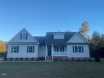 Nestled in Spring Hope at 529 Mulberry Road, this single-story light gray house features a dark roof, inviting front porch, and charming upper dormer, all set on a grassy lawn with trees beneath a clear blue sky.