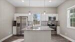 Modern kitchen with white cabinets, stainless steel appliances, granite countertops, a center island with sink, tile backsplash, pendant lights above the island, and a large window letting in natural light.