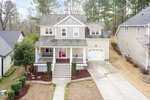 A two-story beige house with white trim at 102 Kipling Drive, Oxford, features a front porch, red door, attached single-car garage, neat lawn, driveway, and tall trees in the background among neighboring homes.