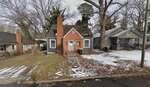 Small brick and wood house with a central chimney at 210 Zollicoffer Avenue, Henderson. Steps lead to the front door, patchy snow covers the ground, bare trees stand in back, and neighboring houses are visible on both sides.