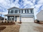 Charming two-story blue house with white trim at 57 Plantation Drive, Youngsville. Features a covered front porch, dark shutters, two-car garage, and a yard with brown grass patches and mulch beds under a partly cloudy sky.