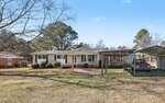 A single-story white house at 774 Abbott Road, Henderson, features a front porch in a spacious yard with scattered trees. A covered carport shelters a red pickup truck on the right, beside a wooden pergola. The sky is clear and sunny.