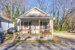 A small single-story house at 621 Marshall Street in Henderson features a front porch with wooden railing, two chairs, and a sloped roof. Sparse grass covers the yard, leafless trees surround the home, and a car is parked on the left side.