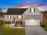 A modern single-story house with a front porch, double garage, and gabled roof, set against a colorful sunset sky with neatly manicured lawn and driveway.