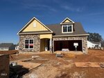 A newly built, two-story house with a mix of stone and yellow siding, a double garage, and a "SOLD" sign in the front window. Construction materials are scattered on the bare, unfinished yard.