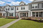 Modern two-story townhouse with light blue and gray siding, white trim, brick accents, large front windows, a covered porch, manicured lawn, and a sidewalk leading to the front entrance.