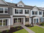 A modern two-story townhouse with gray and white siding, brick accents, large windows, a covered front entry, and neatly landscaped shrubs and grass.