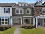A modern two-story townhouse with green and white siding, brick accents, and a covered front porch, surrounded by small shrubs and mulch, between two similar homes.