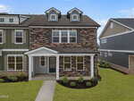 A two-story townhouse with a brick and stone exterior, white trim, and a covered front porch. Well-kept landscaping and neighboring homes are visible on either side under a clear blue sky.