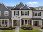 A two-story townhouse with a brick and siding exterior, blue shutters, a covered entryway, and neatly landscaped front yard, set against a bright blue sky with scattered clouds.