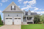 A modern two-story house with gray siding, white trim, black shutters, and a double garage. A small porch with white railings is at the entrance, and the front yard features green grass and a few trees.