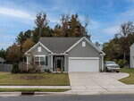 Single-story gray house with white trim, two-car garage, and front porch. Well-kept lawn and small tree in front yard; white pickup truck parked in driveway. Trees with autumn leaves are visible behind the house.