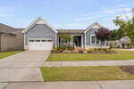 Single-story blue house with white trim, a two-car garage, front porch with white railings, landscaped yard, and a driveway leading to the street; trees and neighboring houses are visible.