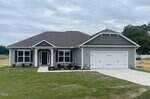 Single-story house with gray siding, white trim, and a dark roof. There are two front-facing gables, multiple windows, a double garage, and a small front porch. The yard has new grass and minimal landscaping.