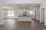 Open-concept kitchen and dining area with wood flooring, white cabinets, stainless steel appliances, pendant lighting over a large island, and windows letting in natural light.