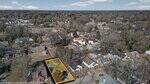 Aerial view of a residential neighborhood with houses, trees, and streets. One rectangular lot, outlined in orange, contains a small house and trees, highlighting the property for sale.