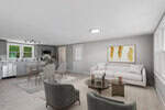 A modern open-plan living and dining area with light gray walls, a white sofa, two green armchairs, glass coffee tables, and a dining table with four chairs. The kitchen with stainless appliances is visible in the background.