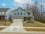 A two-story blue house with white trim, a covered front porch, and an attached two-car garage. The front yard has minimal landscaping and a concrete driveway. A white barrier labeled "Ryan" is placed at the end of the driveway.