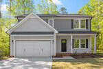 Two-story suburban house with light gray siding, dark gray accents, and a black shingled roof. There is a double garage, a covered entryway, and white-trimmed windows. Trees and greenery surround the property.