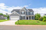 A two-story gray suburban house with white trim, a double garage, covered front porch, and manicured lawn, set under a blue sky with some clouds.