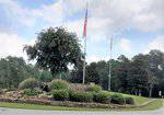 A stone sign reading "Lake Royale" sits among landscaped bushes, a small waterfall, and flagpoles displaying the American and North Carolina flags, with trees and a cloudy sky in the background.