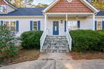 A house with light-colored siding, blue shutters, a blue front door with a wreath, white railings, and a stone staircase leading to the entrance; bushes and a concrete walkway are in front.