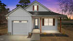 A single-story white house with a gable roof, attached one-car garage, front porch with wooden posts, brown shutters, and a concrete driveway, photographed at dusk with a purple and orange sky in the background.